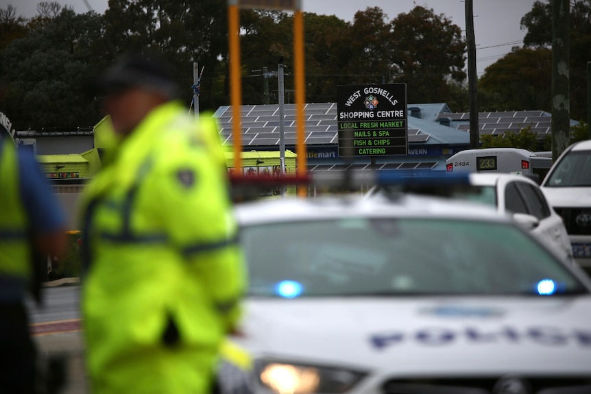 A police officer and a police car out-of-focus in the foreground with West Gosnells Shopping Centre in the distance.