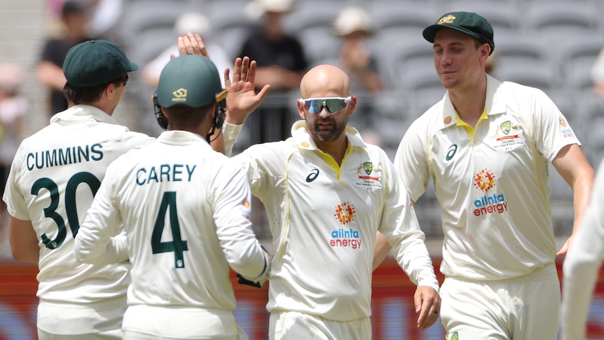 Nathan Lyon hold sup his hand as other men gather around him