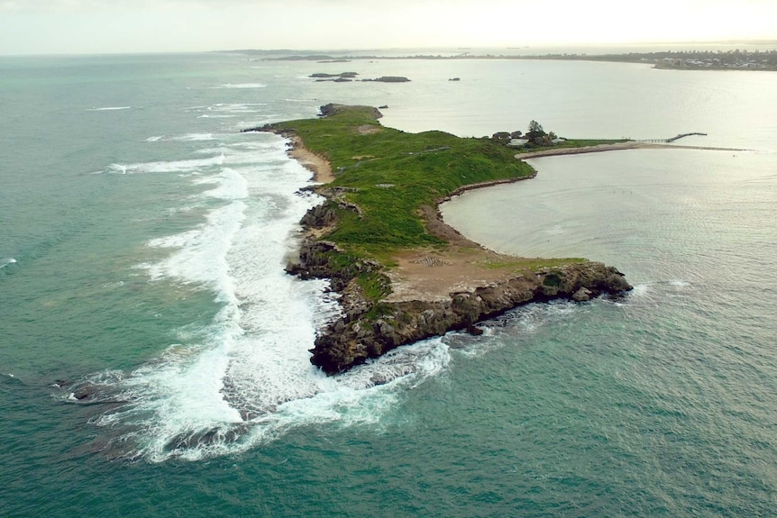 An aerial shot of an island with ocean waves breaking to one side.
