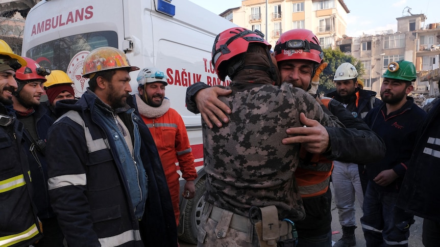 Rescuers hug each other beside ambulance.