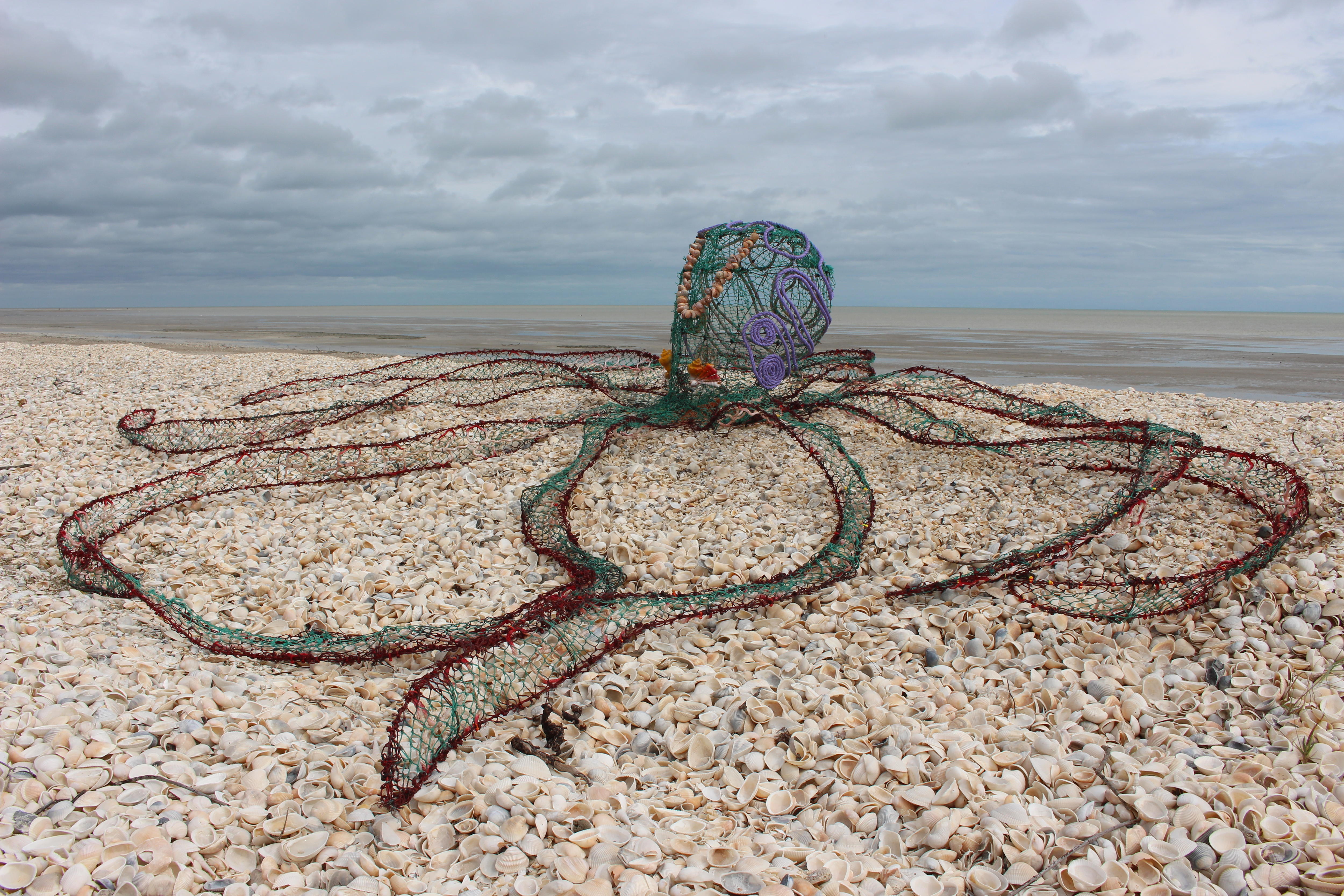 A large octopus sculpture is sprawled out across a beach. 