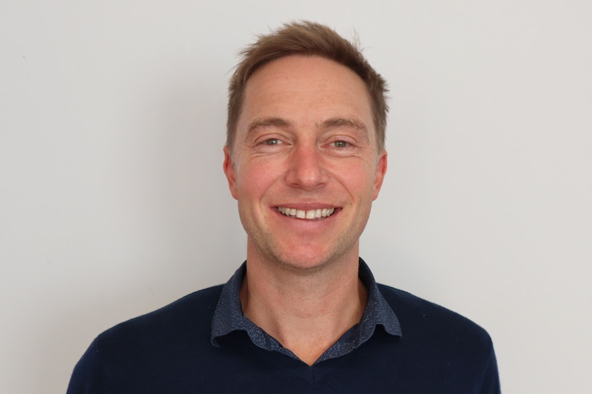 A man with short brown hair smiling with a blue shirt 