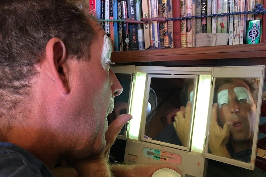 A man looks into a mirror to apply face paint