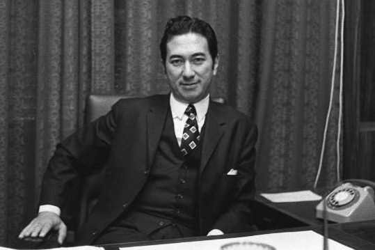 a black and white photo of a man in a suit sitting behind a desk