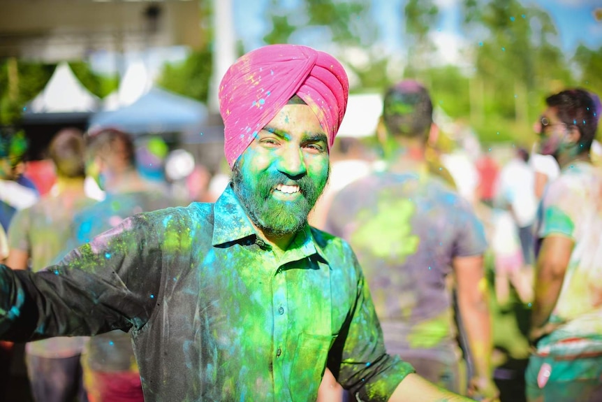 A man wearing a turban and covered in coloured powder stops to enjoy Holi celebrations at Brisbane's Festival of Colours