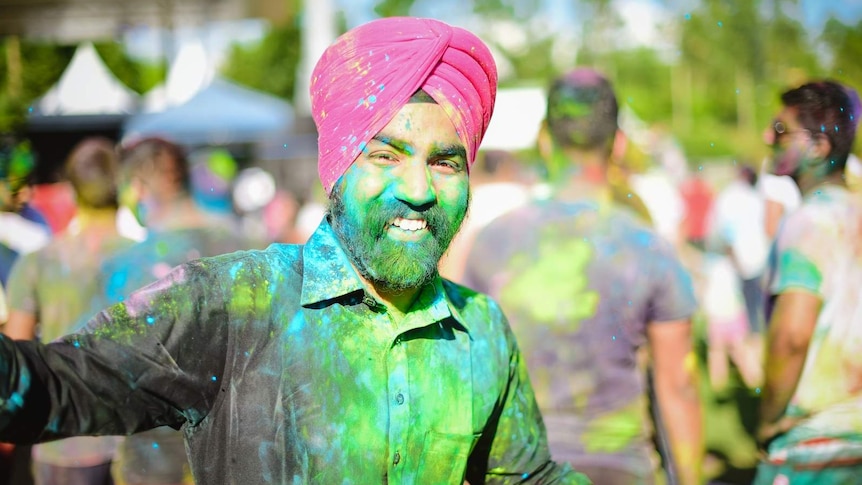 A man wearing a turban and covered in coloured powder stops to enjoy Holi celebrations at Brisbane's Festival of Colours