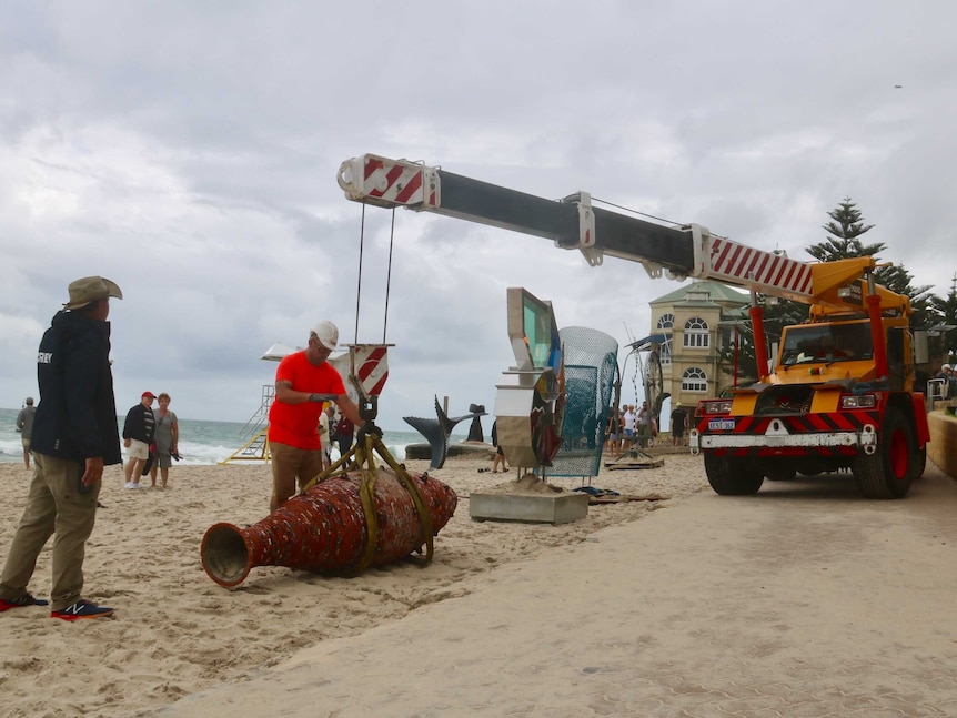 A crane moves a sculpture on the beach
