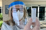 A healthcare worker in PPE holds with a rapid antigen test.