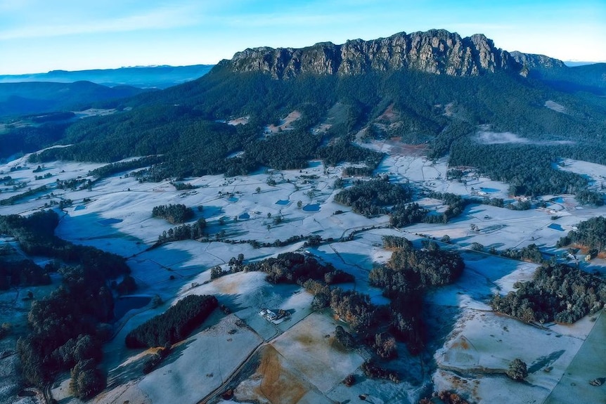 A large mountain and land around is covered in white frost as seen from plane height.