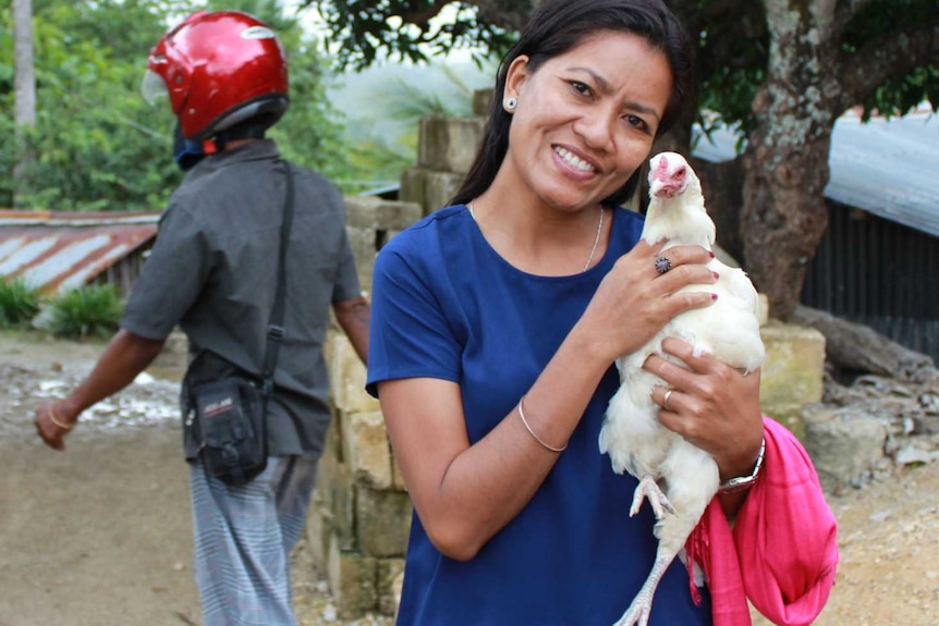 East Timorese man holds a white hen in the village of Saburai, East Timor