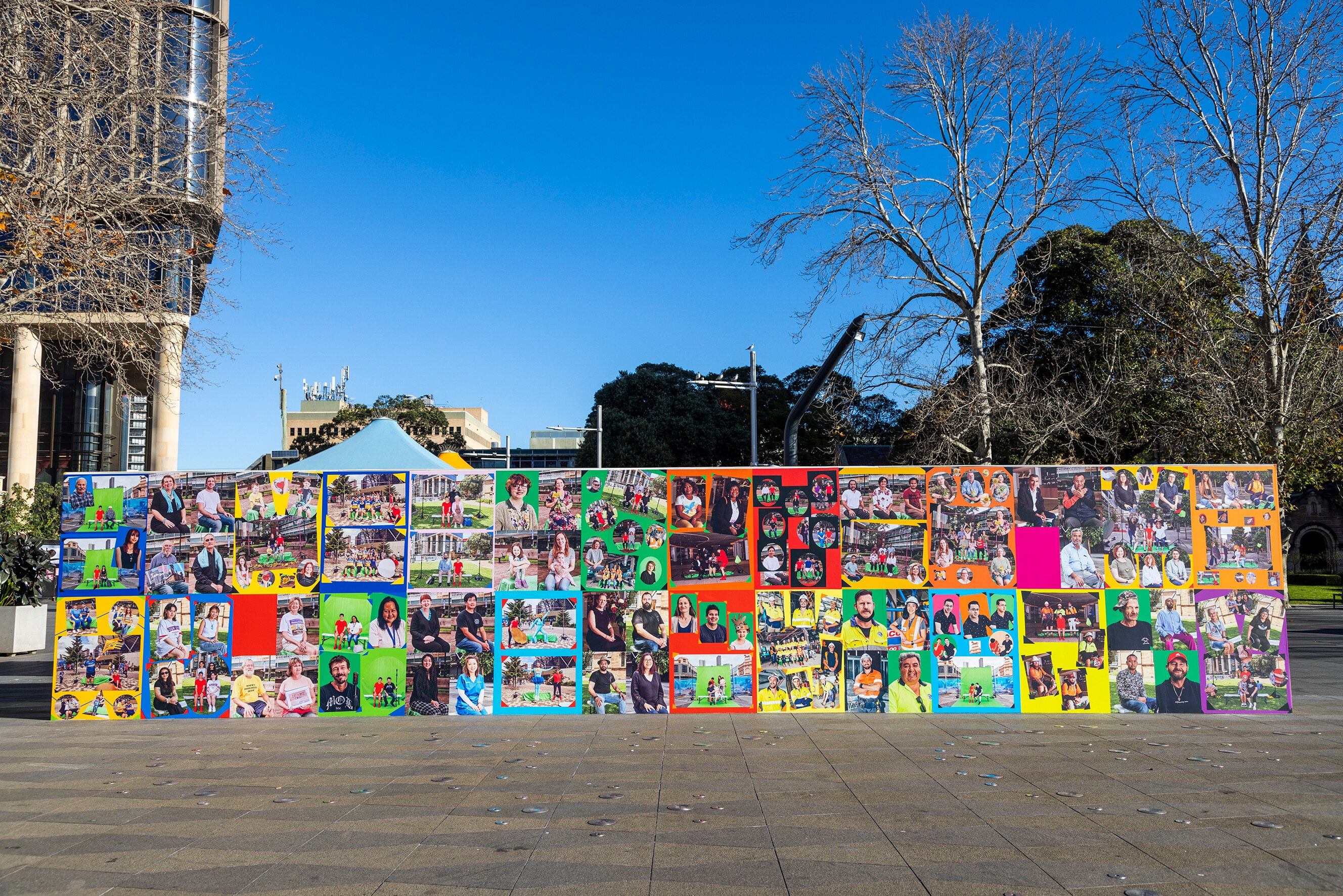 A wall of photos and collages in a public square with deep blue skies.