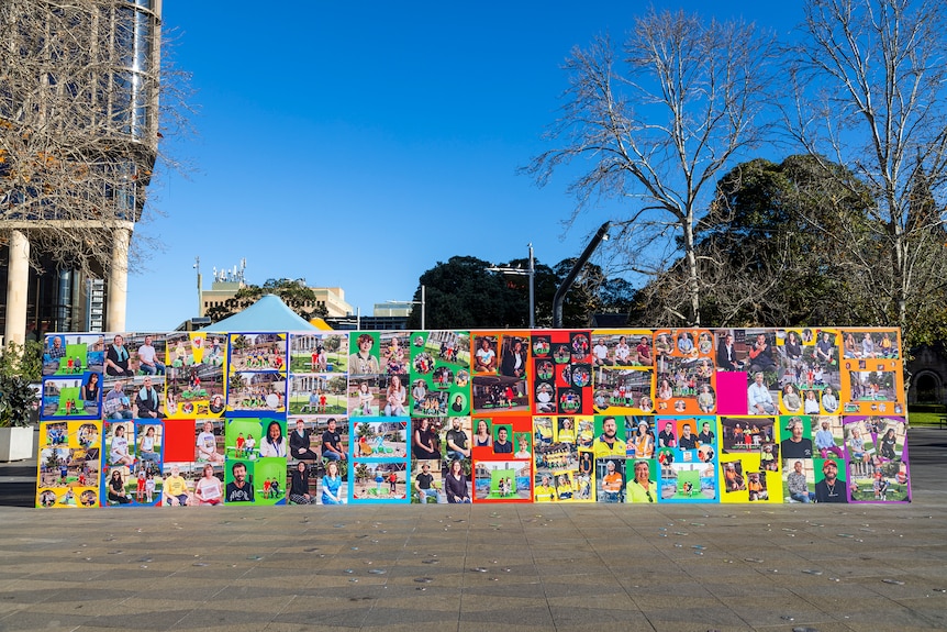 A wall of photos and collages in a public square with deep blue skies.