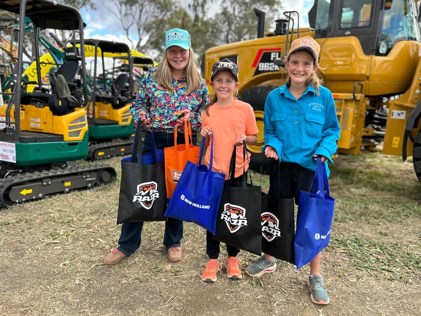 three girls stand with sample bags in front of a large tractor