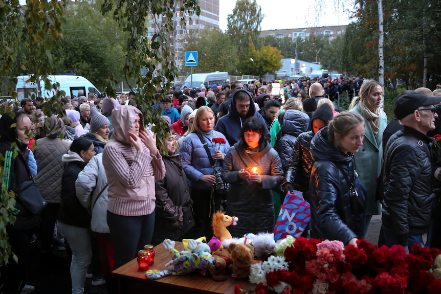 People gather to lay flowers, one young man holds a candle.
