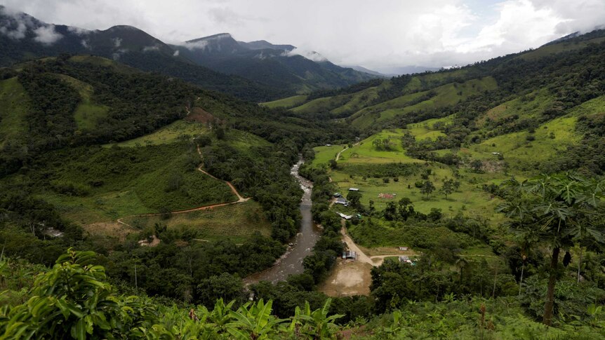 A large brown river curves through a verdant valley with foothills continuing into the distance