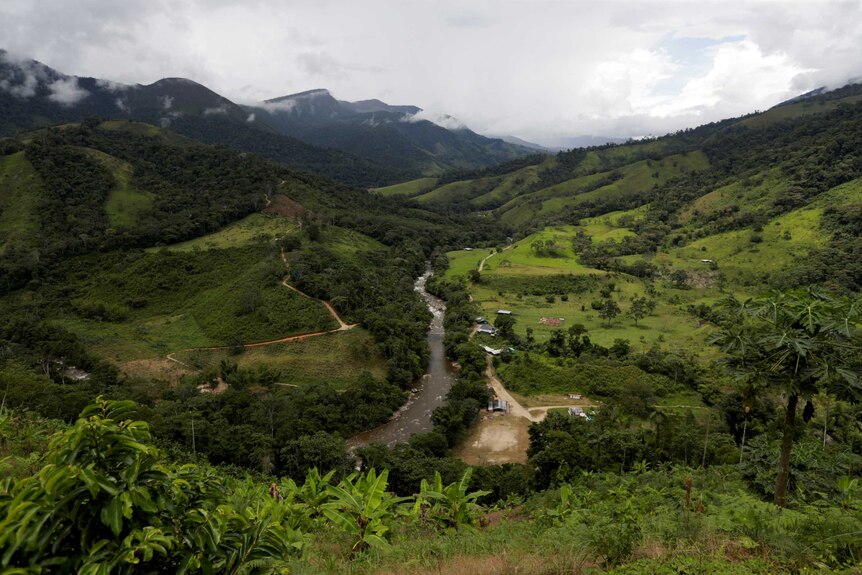 A large brown river curves through a verdant valley with foothills continuing into the distance