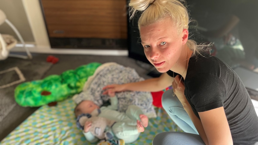 Mum plays with baby, laying on a mat.