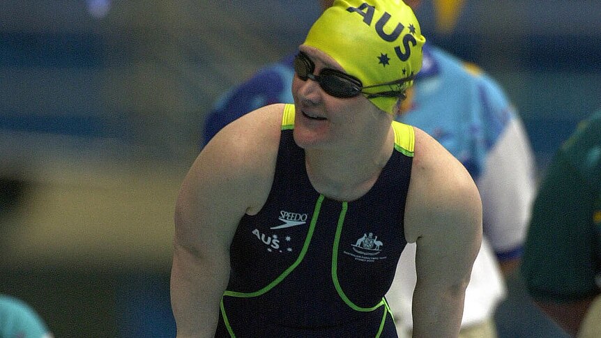 A short-statured woman wearing an Australia swimming cap and costume and standing on the blocks.