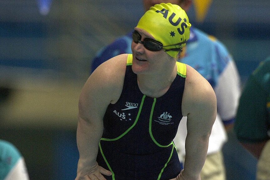 A short-statured woman wearing an Australia swimming cap and costume and standing on the blocks.