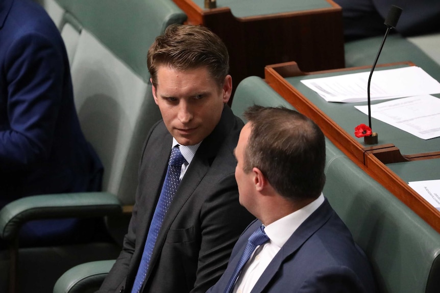 View of the head and shoulders of Andrew Hastie a green seat looking into the face of a male colleague seated next to him
