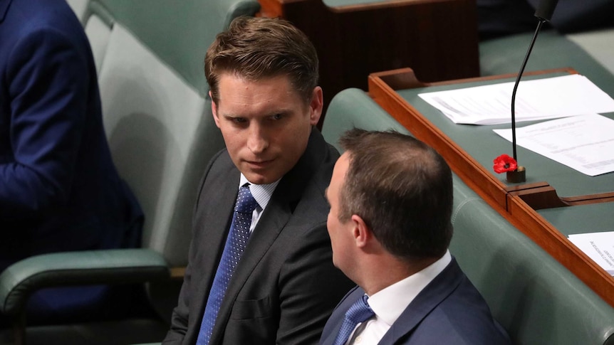 View of the head and shoulders of Andrew Hastie a green seat looking into the face of a male colleague seated next to him