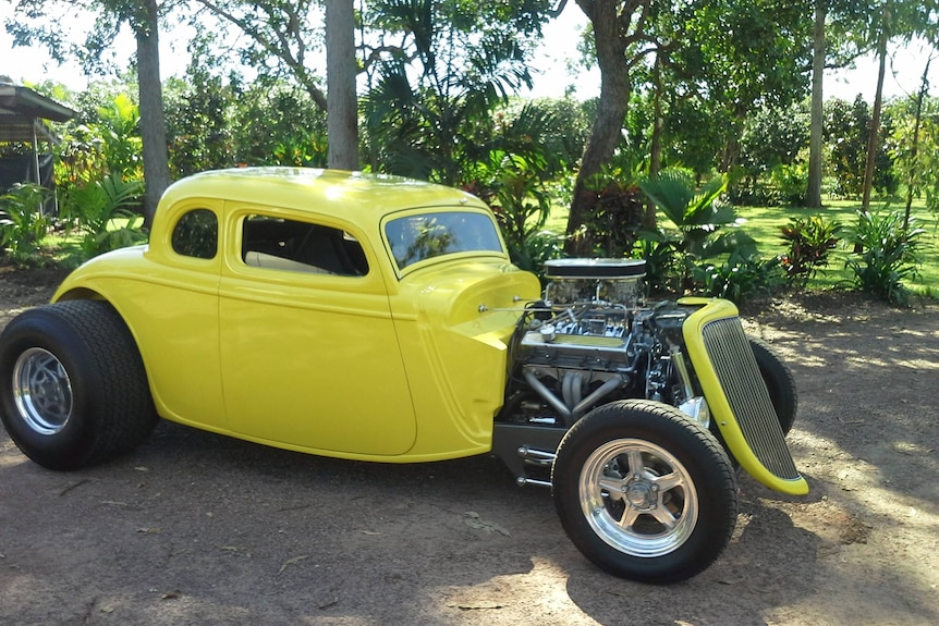 A sleek and yellow bulky car sits amongst green trees