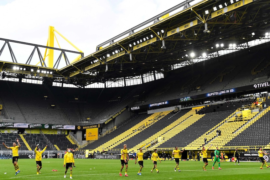 Borussia Dortmund players stand inside an empty stadium at the end of a Bundesliga match.