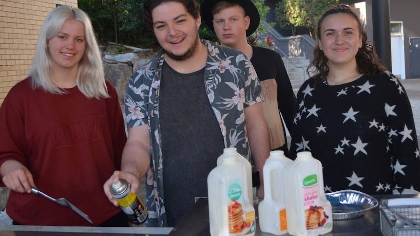 Four people smiling to the camera as they cook at a barbecue