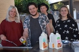 Four people smiling to the camera as they cook at a barbecue