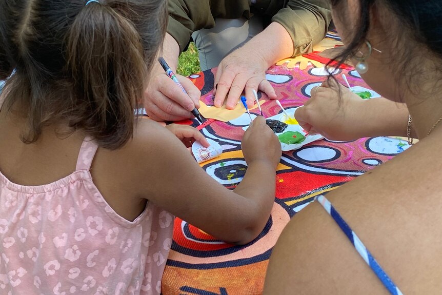 A child's hand holds a small paint brush with two adult arms in frame also painting circles