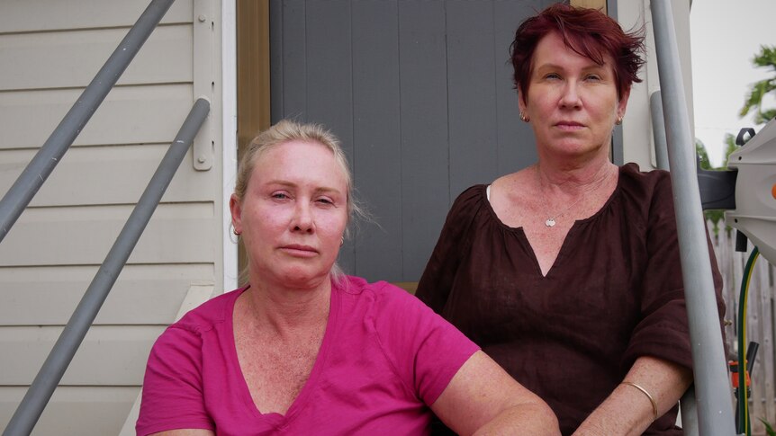 Two middle aged women sitting on the front stairs of a Queenslander style home. 