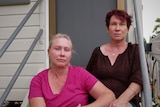 Two middle aged women sitting on the front stairs of a Queenslander style home. 