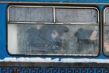A passenger wearing a protective face mask is seen through a frost-covered bus window.