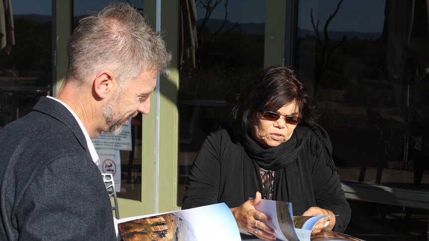 A white man and an Indigenous woman sit at a table looking at brochures.