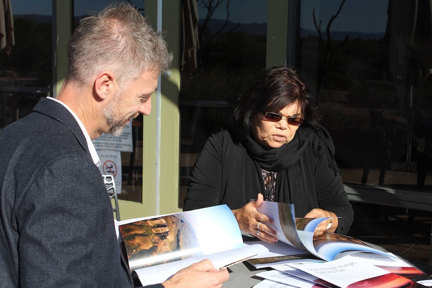 A white man and an Indigenous woman sit at a table looking at brochures.