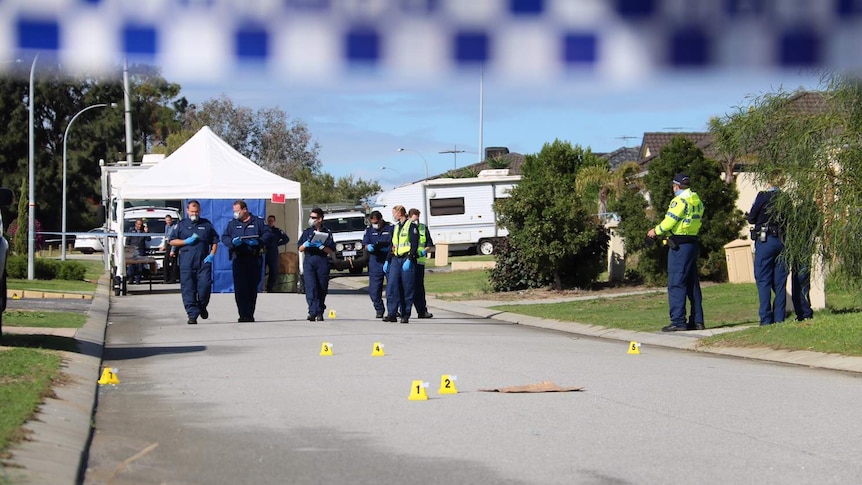 Detectives and forensic officers walk along a road at the scene of a triple shooting in Perth's north