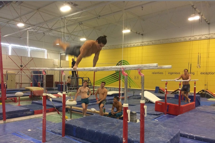 One gymnast performs a routine while others watch on.
