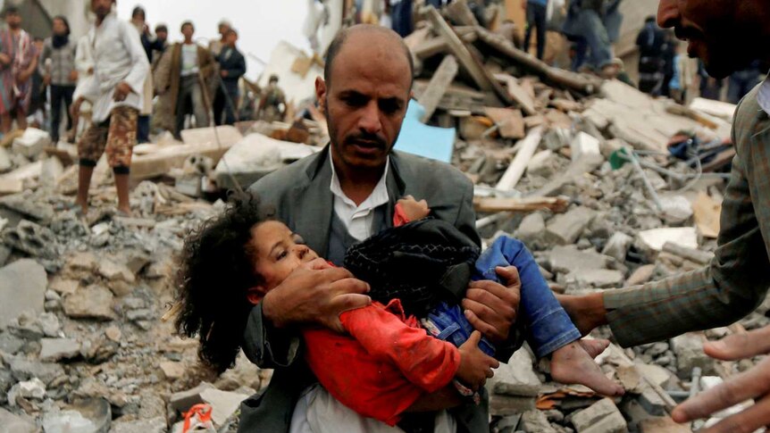 A man carries a young girl through rubble after an air strike in Yemen.