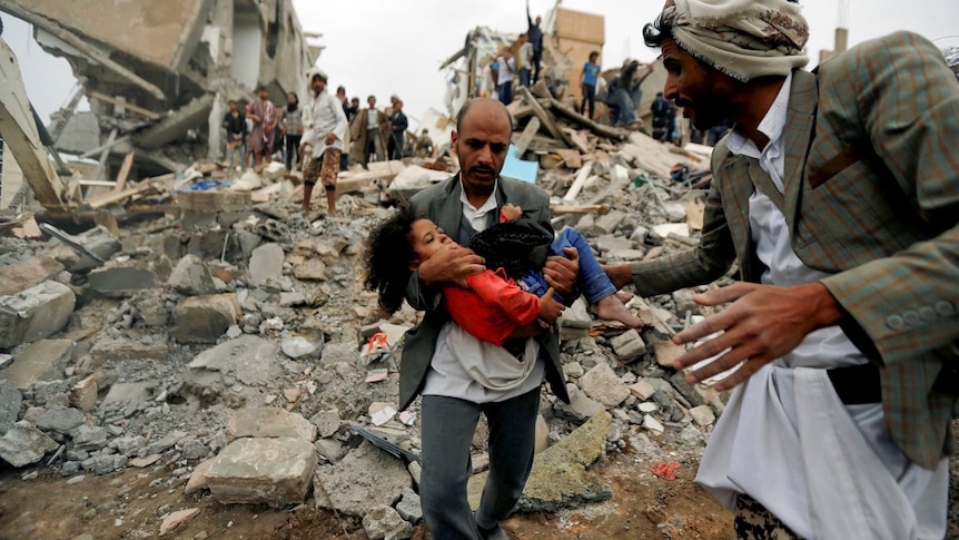 A man carries a young girl through rubble after an air strike in Yemen.