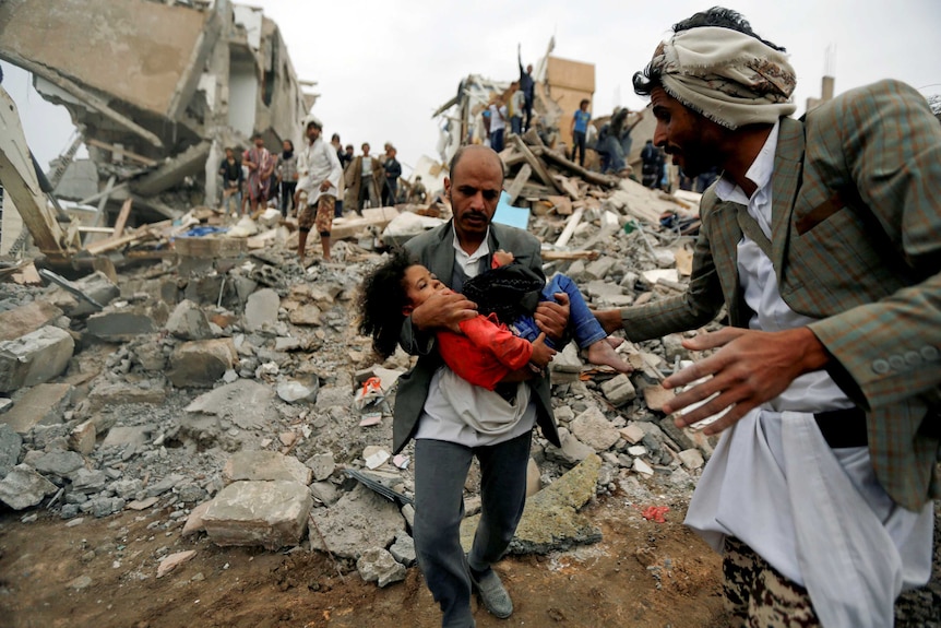 A man carries a young girl through rubble after an air strike in Yemen.