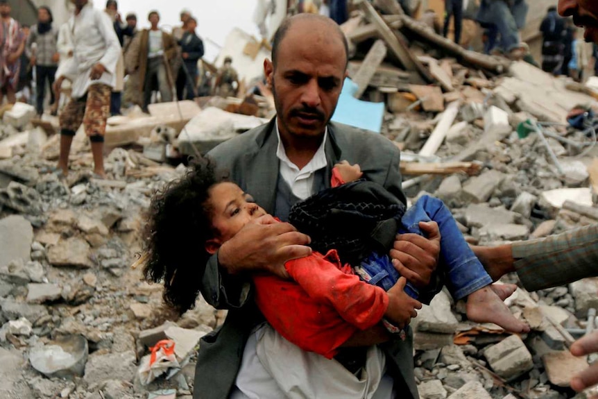 Un bărbat poartă o fată printre dărâmături după un atac aerian în Yemen.