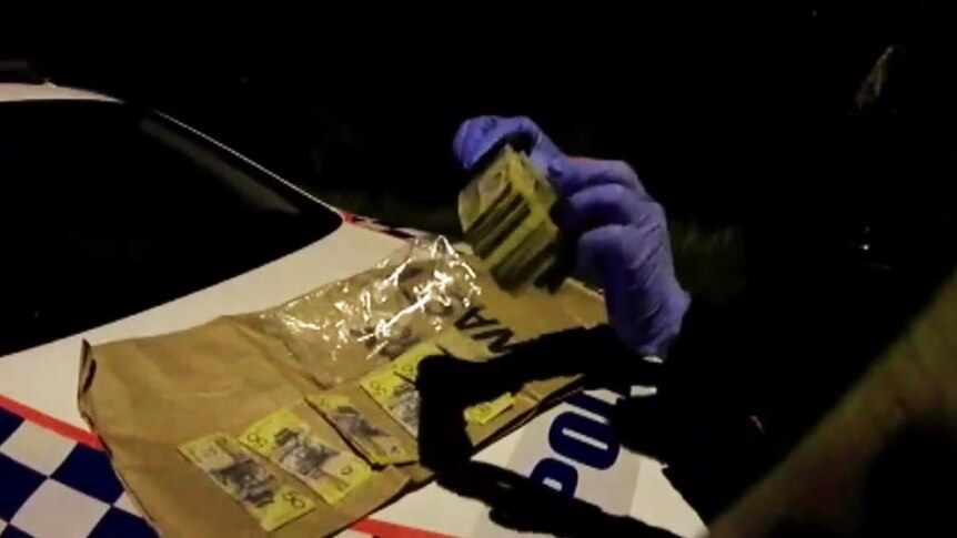 A police officer spreads a large wad of cash across the bonnet of a police car