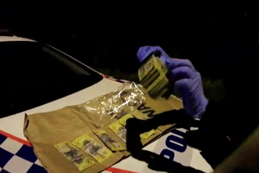 A police officer spreads a large wad of cash across the bonnet of a police car