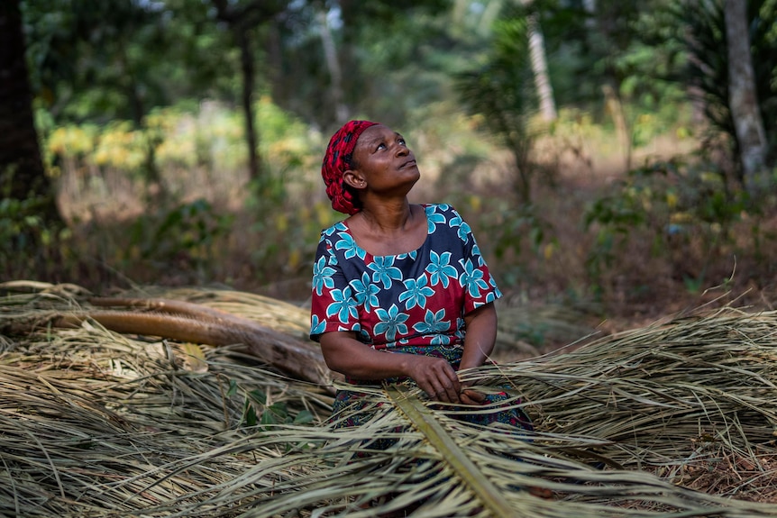 An African women looks up to the sky as she knits palm leaves. 