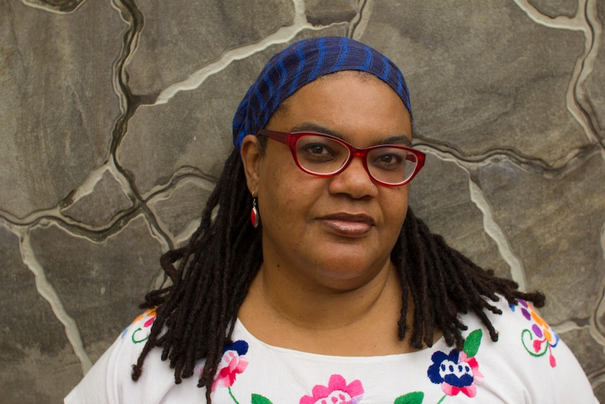 Dr Natasha Gordon-Chipembere with shoulder-length hair, blue headband and glasses, smiles slightly.