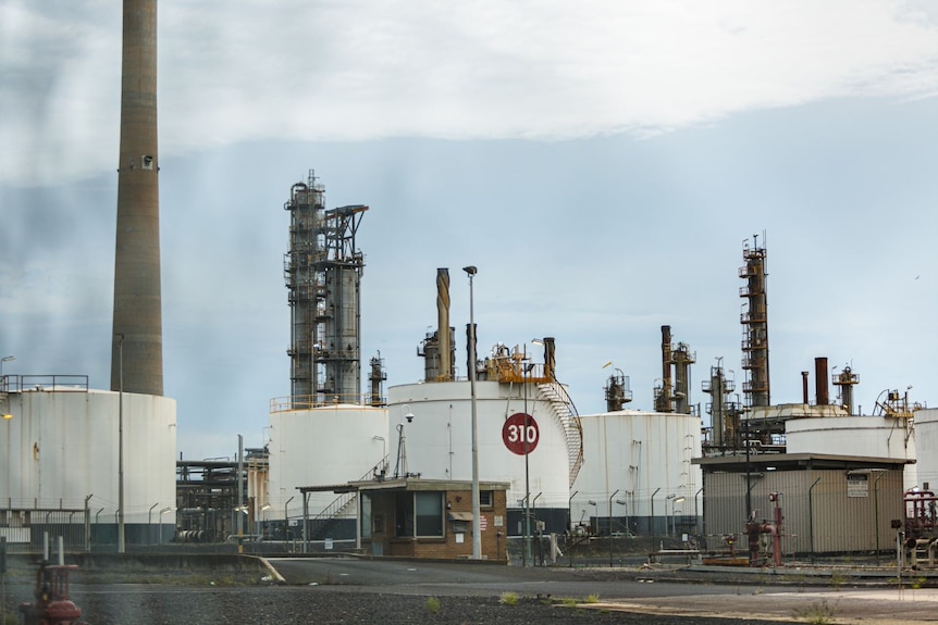 Large white tanks sit in the refinery with a chimney behind them