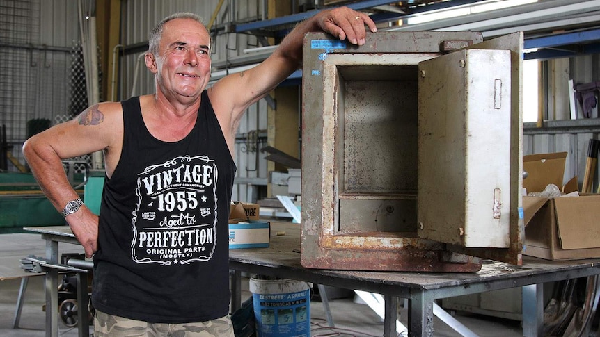 a man smiling next to an old empty safe