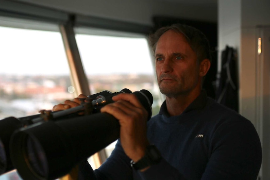A man in a control tower holding a large pair of binoculars.