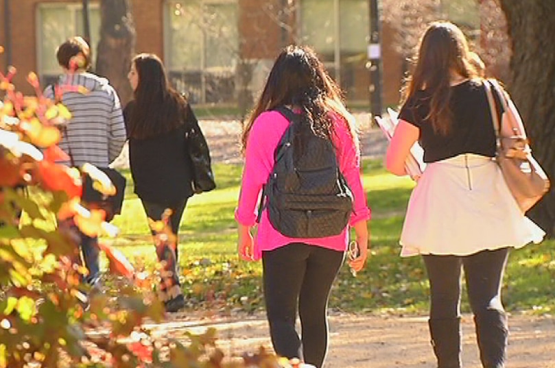 University students walk through a campus, with autumn leaves on the left.