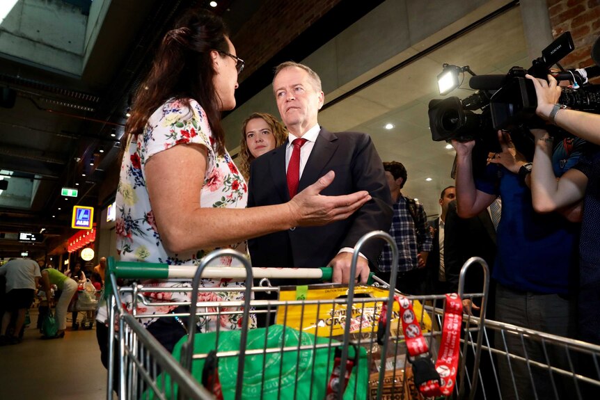 Bill Shorten puts one hand on a shopper's trolley as she holds her hands in a shrug position